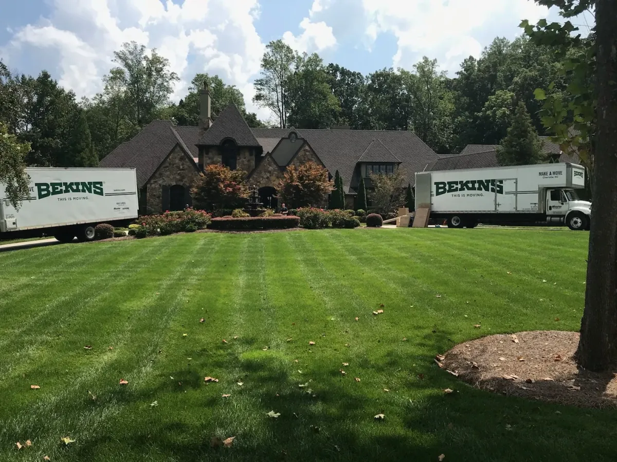 Two Bekins moving trucks at a stone home in Charlotte